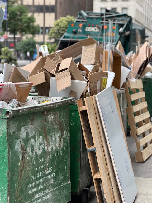 A collection of mixed waste materials piled against a brick wall adjacent to a concrete block wall in an outdoor setting. The rubbish includes several flattened cardboard boxes, a large fabric or plastic bag, and loosely scattered paper and packaging materials. The surface on which the waste rests is uneven, composed of dirt and small stones, with a tree trunk partially visible on the left side of the image. The scene is lit with natural daylight, highlighting the textures of the debris and surrounding surfaces. This type of scene illustrates a typical instance of waste accumulation that may be addressed through private rubbish removal services such as those offered by Rubbish Removal Paddington, which specialize in on-site clearance and alternative waste handling options rather than relying solely on municipal rubbish collection.